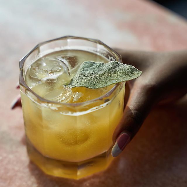 Golden cocktail garnished with sage